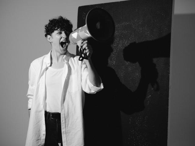 A young person stands with their mouth open and a megaphone in front of their face in black and white